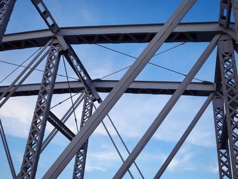 Detail shot of an historic gray painted Dutch riveted truss bridge against a blue sky.