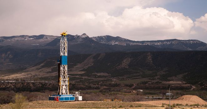 An oil derrick stands late in the day against the mountains