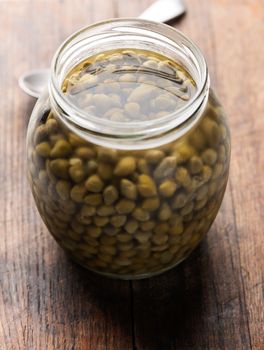 Pickled capers in glass jar on wooden background