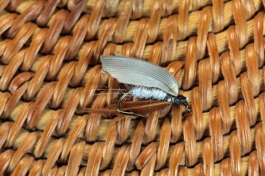 Macro photo of an artificial fly for fly fishing on a basketwork background.