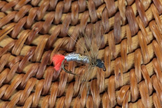 Macro photo of an artificial fly for fly fishing on a basketwork background.