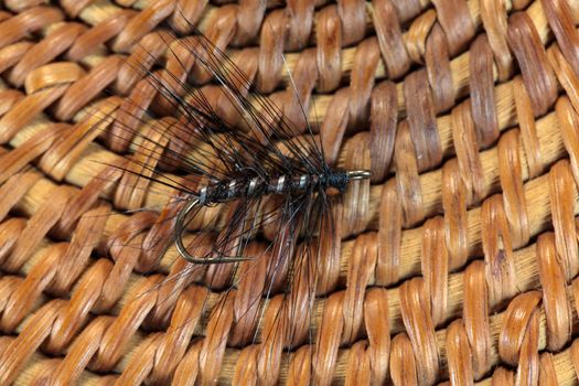 Macro photo of an artificial fly for fly fishing on a basketwork background.