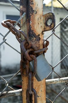 Padlock closed and joined a rusty and old chain. It is possible to appreciate a grill