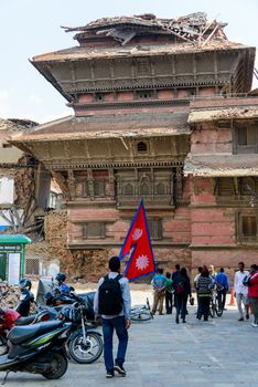 KATHMANDU, NEPAL - MAY 14, 2015: A man carries a large Nepal flag on Durbar Square, a UNESCO World Heritage Site.