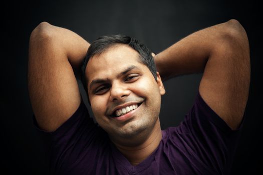 Handsome Indian man happily laughing with joining their hands on back head