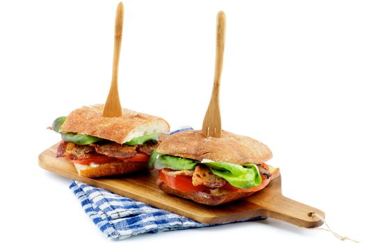 Ciabatta Sandwiches with Bacon, Tomato, Lettuce and Sauces on Cutting Board Arranged with Wooden Fork isolated on white background