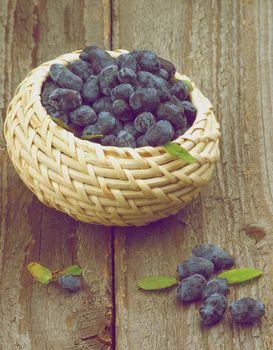 Fresh Ripe Honeysuckle Berries with Leafs in Wicker Bowl on Rustic Wooden background. Retro Styled