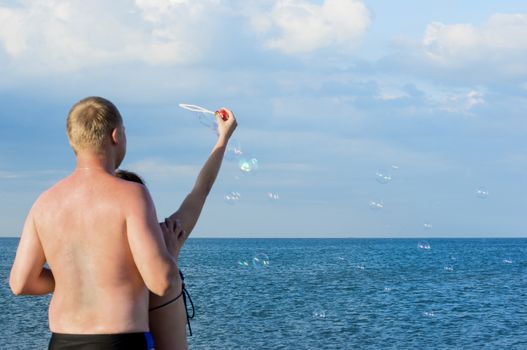 The guy and the girl start soap bubbles on the sea.