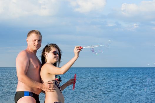 The guy and the girl start soap bubbles on the sea.