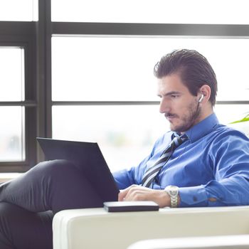 Busy, focused businessman in office working on his laptop wearing headphones. Side view. 