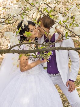 groom and bride in white dress on a background of flowering trees