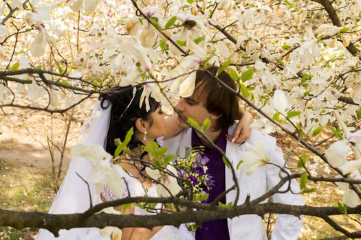 groom and bride in white dress on a background of flowering trees