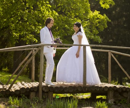 Happy bride and groom on a wooden bridge in the park at the wedding walk