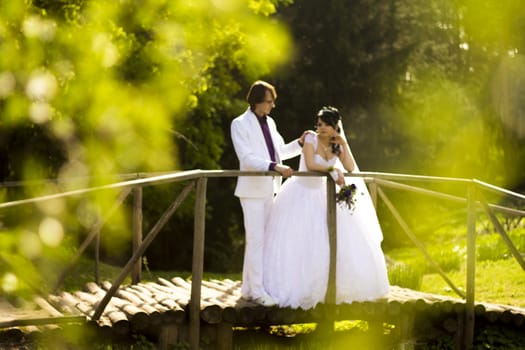 Happy bride and groom on a wooden bridge in the park at the wedding walk