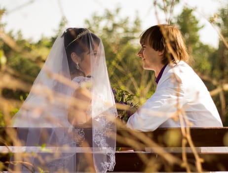 Romantic wedding couple sitting on a bench in the park.