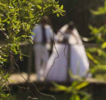 An out of focus bride and groom walk through a bridge with flowers and trees after their wedding