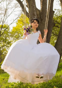 Portrait of a beautiful bride in white wedding dress sitting on swing outdoors