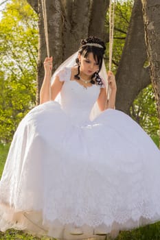 Portrait of a beautiful bride in white wedding dress sitting on swing outdoors