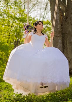 Portrait of a beautiful bride in white wedding dress sitting on swing outdoors