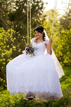 Portrait of a beautiful bride in white wedding dress sitting on swing outdoors
