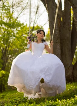 Portrait of a beautiful bride in white wedding dress sitting on swing outdoors