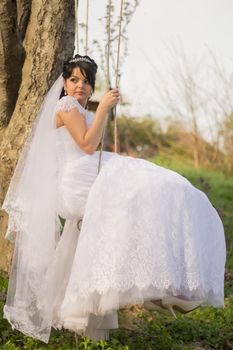 Portrait of a beautiful bride in white wedding dress sitting on swing outdoors