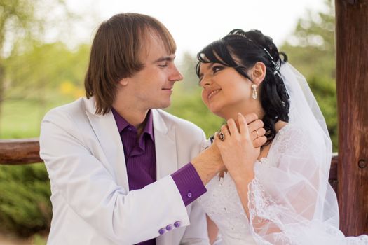 Couple in love bride and groom posing sitting on wooden bench in gazebo in their wedding day in summer.