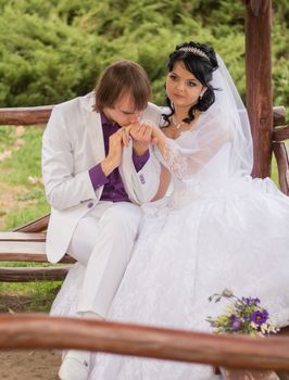 Couple in love bride and groom posing sitting on wooden bench in gazebo in their wedding day in summer.