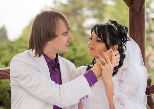 Couple in love bride and groom posing sitting on wooden bench in gazebo in their wedding day in summer.