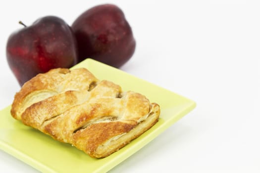 Baked apple strudel on light green plate with 2 red apples behind.  Horizontal image with white copy space. 