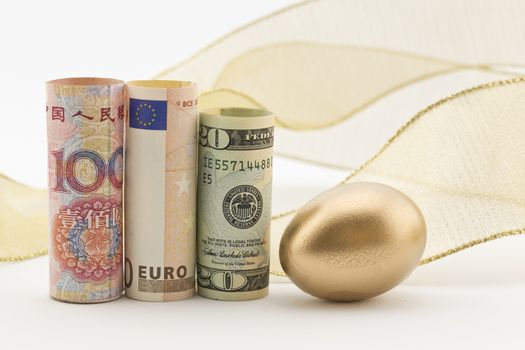 Three major currencies with gold egg and flourish of ribbon reflect savvy business investments, savings, and collaboration on a global scale. 