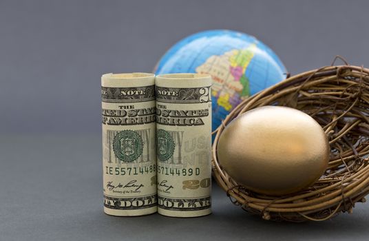 American dollars and gold nest egg with globe in sophisticated, gray background.  Success suggested by global investment and worldwide financial business. Selective focus on key, front metaphors. 