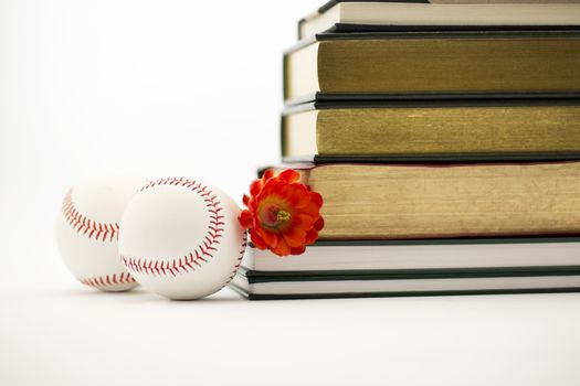 Two baseballs placed with red flower and stack of books depicts positive union of sports and education