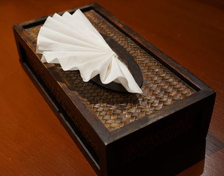 White tissue paper was nicely decorated in tissue box on wooden table.                           