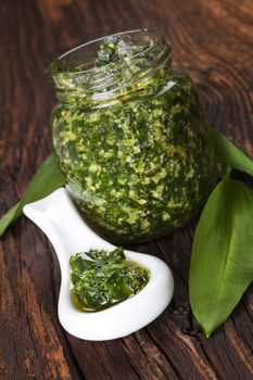 Garlic pesto with fresh wild garlic leaves on brown wooden textured background. Culinary healthy eating. 