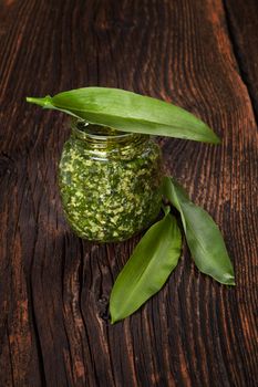 Garlic pesto with fresh wild garlic leaves on brown wooden textured background. Culinary healthy eating. 