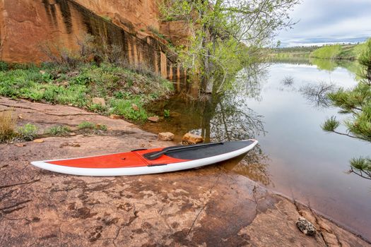 red stand up paddleboard  with a paddle on rocky lake shore - Horsetooth Reservoir, Fort Collins, Colorado