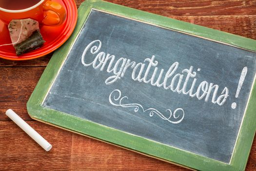 Congratulations! Text on a slate blackboard with chalk and cup of tea