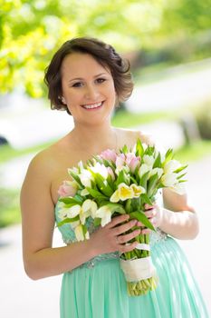 Portrait of a beautiful woman in green dress holding a colorful bouquet of tulips.