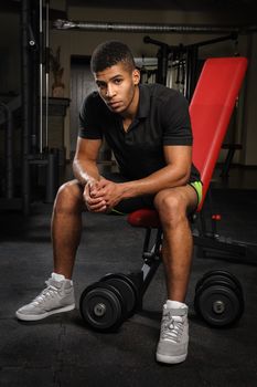 handsome young african descent mixed race man sitting and resting on bench in gym