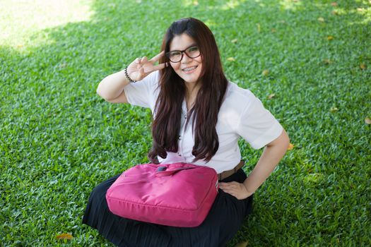 Female student sitting on the lawn. Pink bag was placed on it.