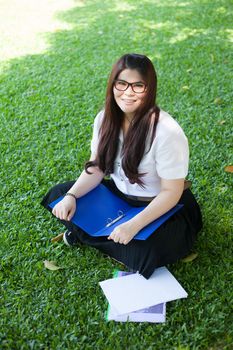 Female student sitting on the lawn. Documents are put on the field
