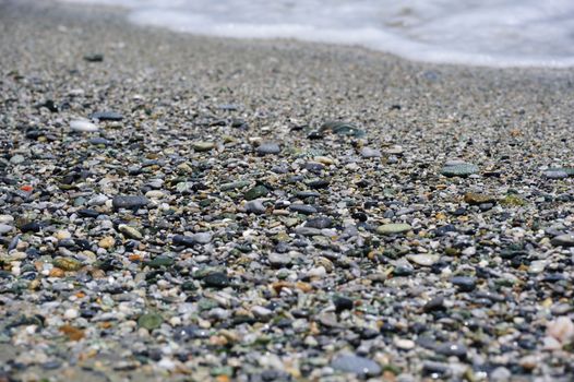 Sea multicolored pebbles, gravel beach in sunlight, selective focus, background