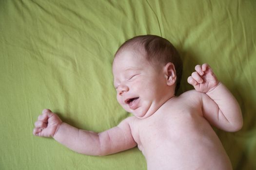 twenty days age baby naked bare crying or smiling close eyes tongue over green sheet bed