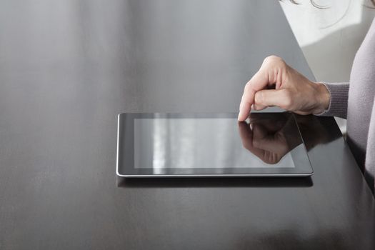 woman hand grey sweater finger touching digital tablet blank screen on black reflect table white curtain indoor