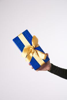 detail of woman arm green dress with a blue and golden gift box in her hands offering
