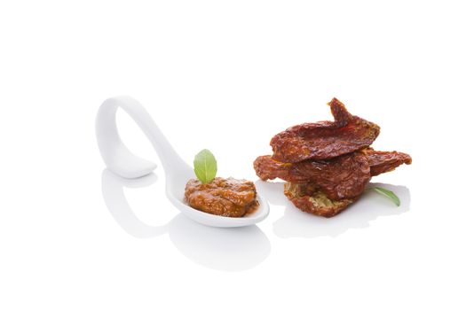 Dried tomatoes and red pesto on spoon with fresh basil leaf isolated on white background. Culinary eating, minimal contemporary styles. 