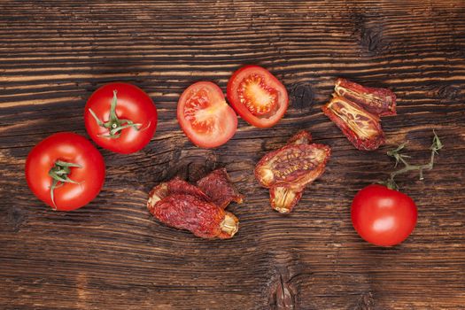 Delicious sundried and fresh tomatoes on brown wooden vintage textured background, top view. Traditional mediterranean kitchen.