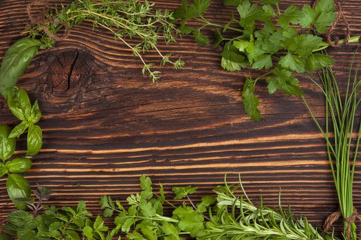 Culinary herbs background with copy space. Fresh basil, cilantro, chive, parsley and mint herbs on brown wooden background with copy space.