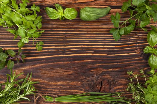 Culinary herbs background with copy space. Fresh basil, cilantro, chive, parsley and mint herbs on brown wooden background with copy space.